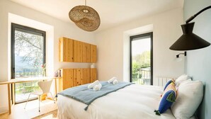 A bedroom with a large bed, a desk with a chair, a hanging light fixture, and large windows. - Villa Côte des Vignes x Annecy 15’ (Charvonnex)