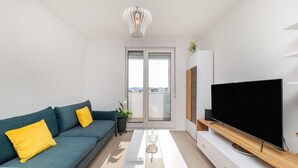 Een moderne woonkamer met een bank, een salontafel, een televisie op een houten standaard, en een balkon met uitzicht.
