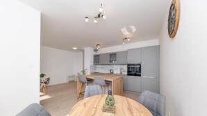 Een moderne keuken met grijze kastjes, een houten eettafel en een hanglamp.