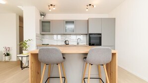 Een moderne keuken met twee barkrukken, een marmeren aanrechtblad en een inbouwoven.