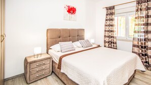 Ein Schlafzimmer mit Bett, Nachttischen, Vorhängen an einem Fenster und einem an der Wand hängenden Kunstwerk.