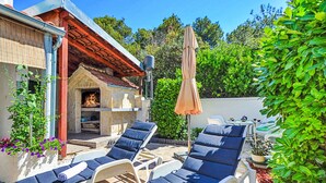 Eine Terrasse mit Liegestühlen, einer Steinkochküche und einer Pergola.