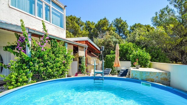 Ein Schwimmbad mit Liegestühlen, einer überdachten Terrasse und üppiger Bepflanzung.