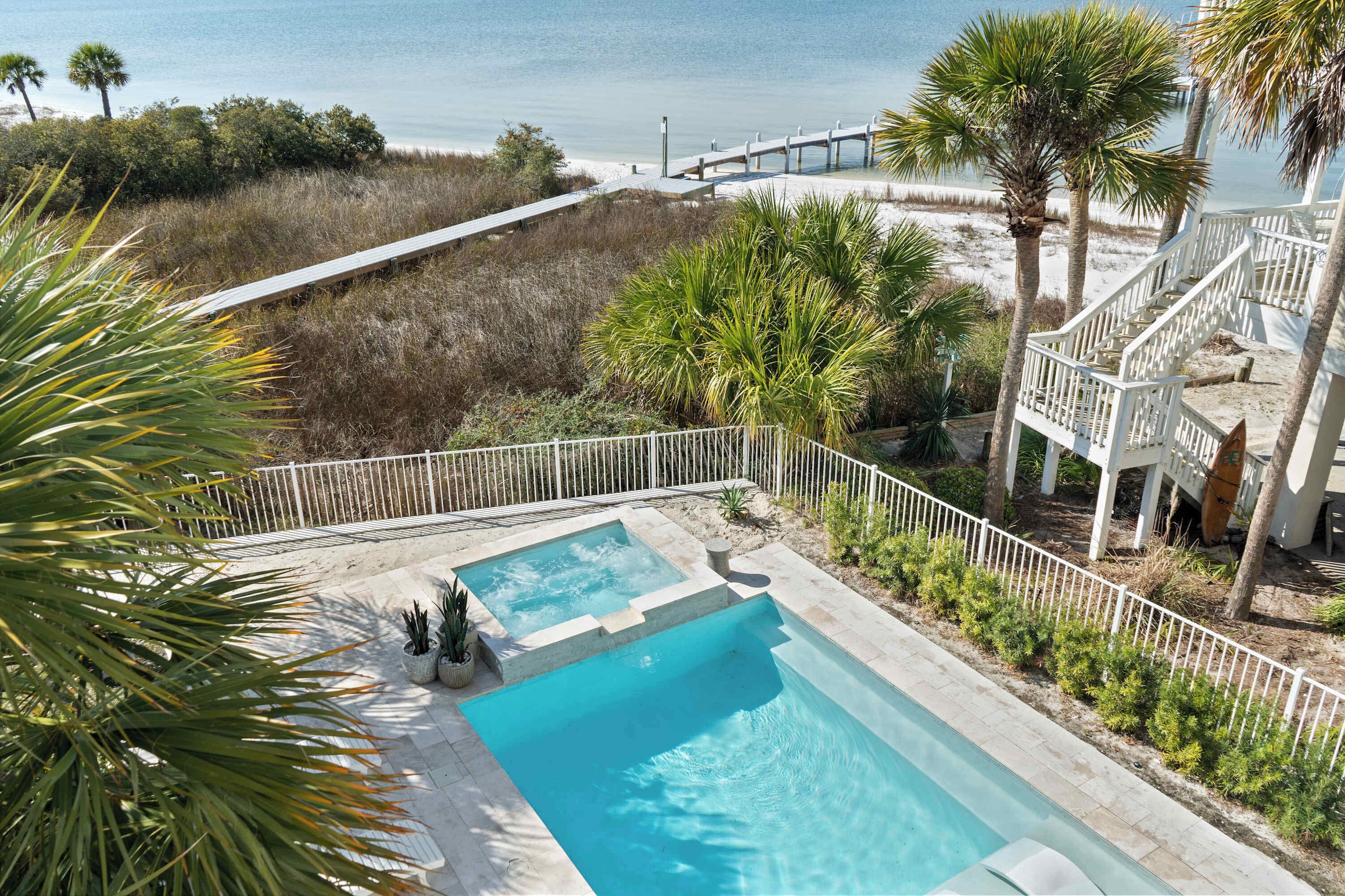 Ein Pool mit Holzterrasse, umgeben von Palmen und Blick auf den Strand.