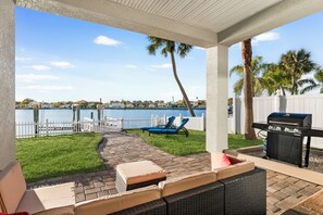 Un porche cubierto con vista a un lago, mobiliario exterior y una parrilla.