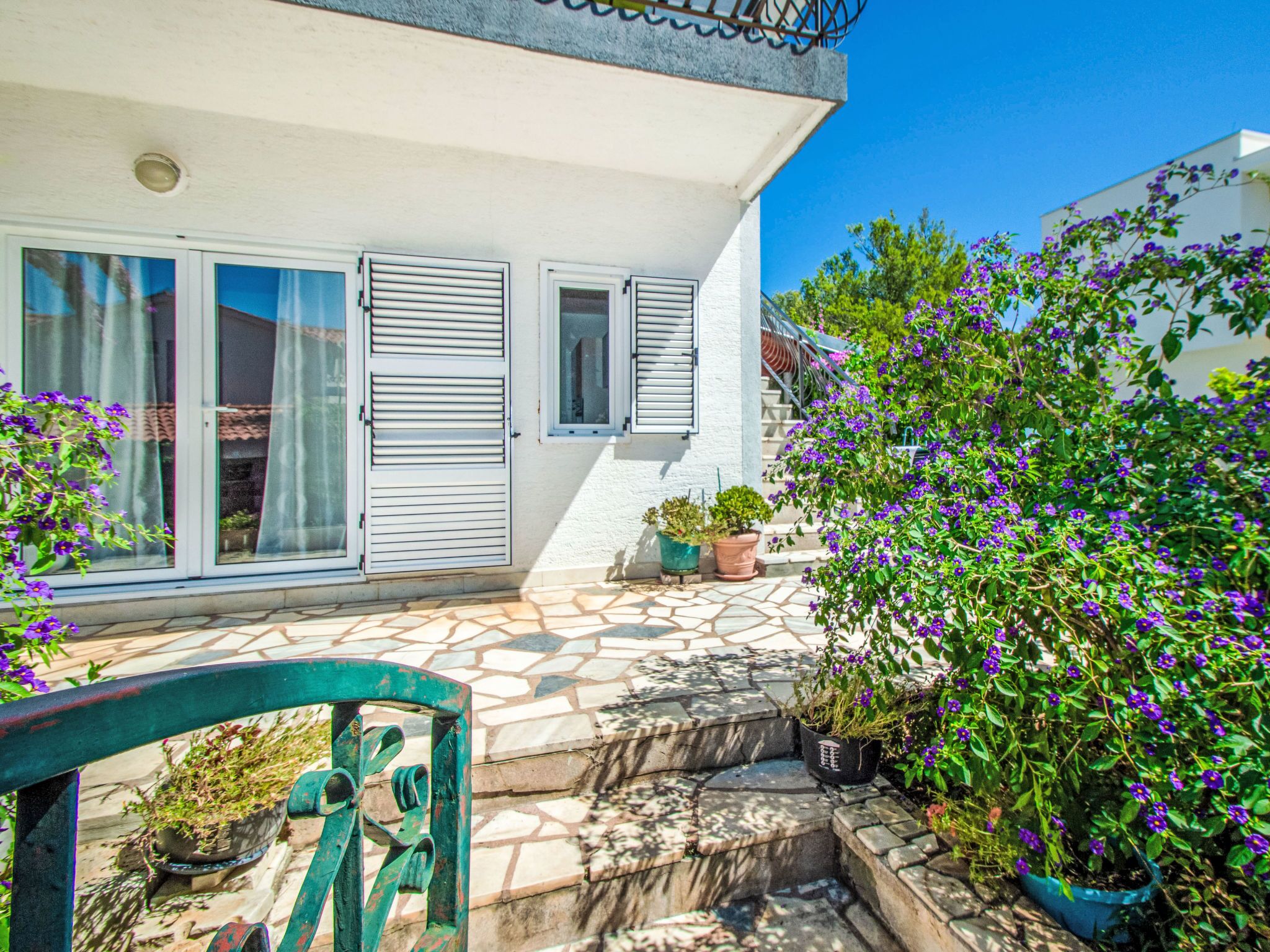 A house with a tiled patio, a green chair, and potted plants.