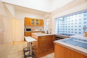 A kitchen with wooden cabinets, a microwave, a stove, and a bar stool. - Cozy little house in the center of Lisbon, with preserved historic architecture. (Lisboa)