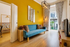 A living room with a blue sofa, a wooden side table, and a television. - A cozy little house in the center of Lisbon, featuring well-preserved historic architecture.   (Lisboa)