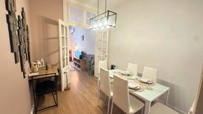 A dining area with a white table set for four, a hanging light fixture, and a view into another room. - A cozy little house in the center of Lisbon, featuring well-preserved historic architecture.   (Lisboa)