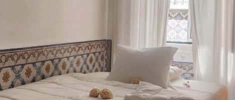 A bedroom with a large bed, white curtains, a hanging light fixture, and a patterned headboard.