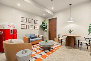 A modern living room with a sofa, coffee table, and a dining area with chairs. There is a Coca-Cola vending machine and framed pictures on the wall. - Condado Modern-Cozy 2-Bedroom City & Sea Getaway (San Juan)