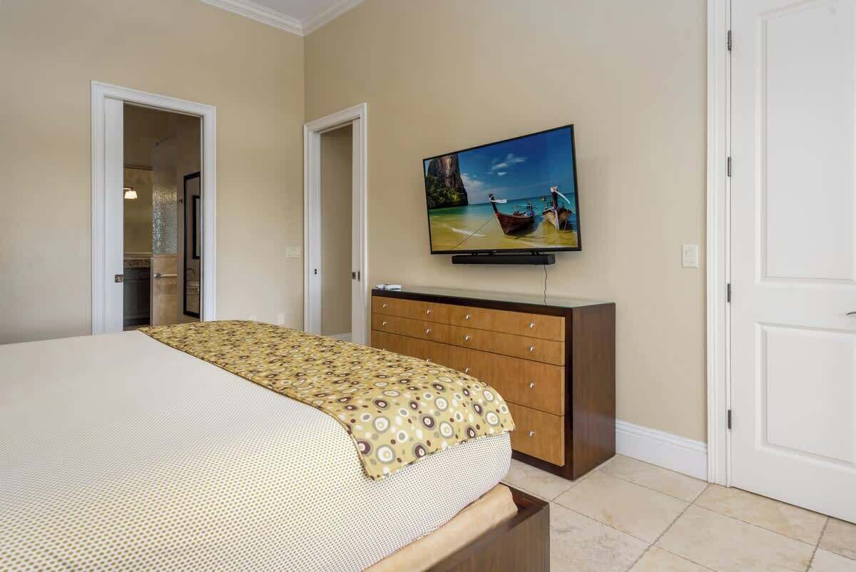 A hotel room with a bed, a TV on the wall, a wooden dresser, and a door.