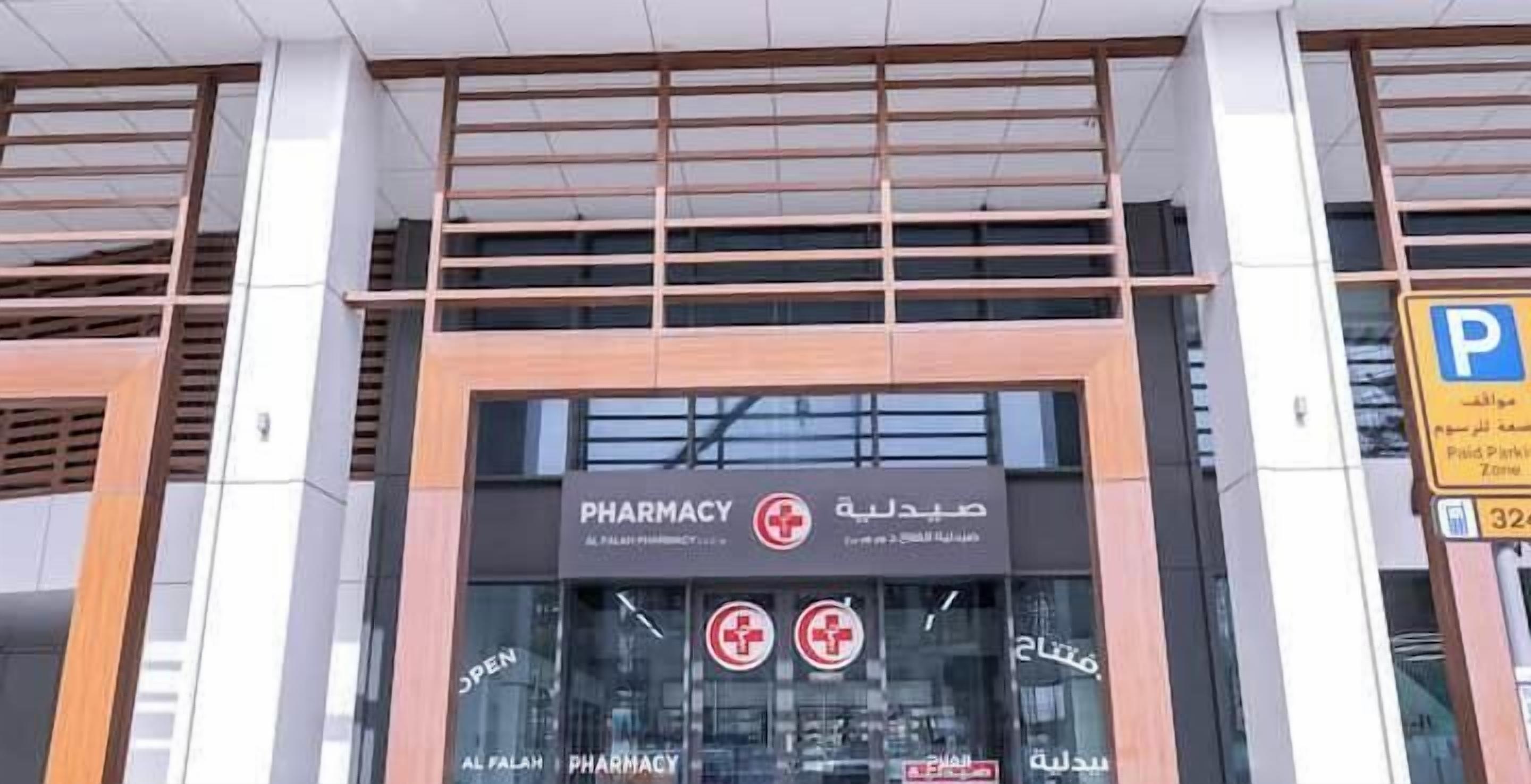 A pharmacy with a sign in Arabic and English, a glass entrance, and a parking sign nearby.