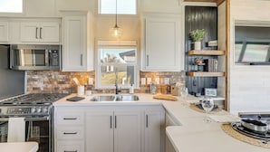 A kitchen with white cabinets, a stainless steel refrigerator, a gas stove, and a window above the sink. - "Cozy Montana" Home w/ Mountain Views! (Kalispell)