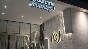 Hotellin sisäänkäynti, jossa on kyltti, jossa lukee ”Coordenada (maa)”, ja seinässä on tyylitelty C-kirjaimen muotoinen logo.