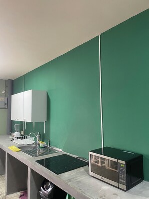 A kitchen with a microwave, sink, and white cabinets. - Hostel YEK (Santa Ana)
