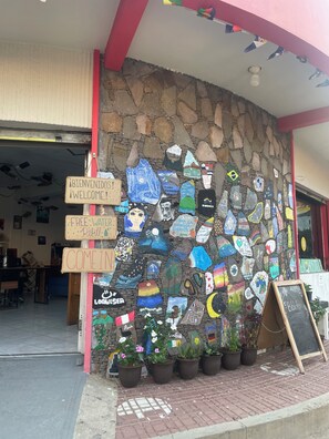 Un mur de pierre orné d’œuvres d’art colorées et de panneaux, avec des plantes en pot et un panneau noir placé à l’extérieur d’un bâtiment.