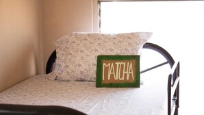 A bed with a floral-patterned pillow and a green sign with 'MATCHA' on it. - Hostel YEK (Santa Ana)