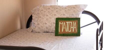 A bed with a floral-patterned pillow and a green sign with 'MATCHA' on it.