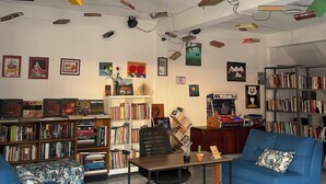 A room with a ceiling-mounted projector system, a central table, two blue sofas, and a bookshelf filled with books. - Hostel YEK (Santa Ana)