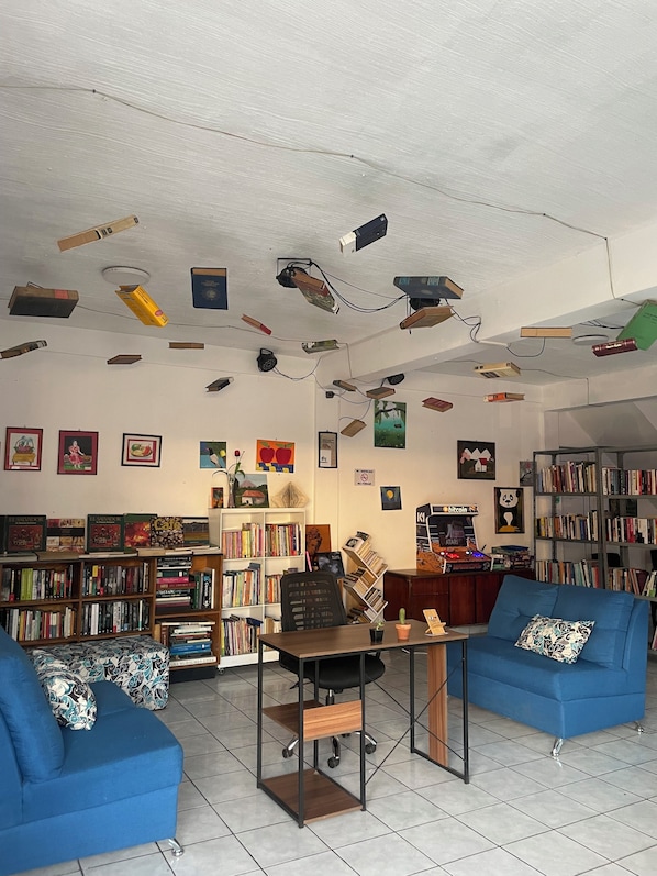 A room with a ceiling-mounted projector system, a central table, two blue sofas, and a bookshelf filled with books.