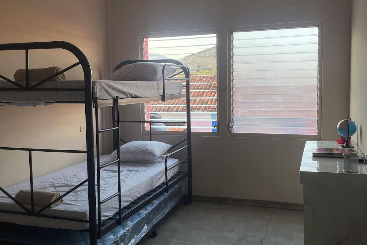 A dormitory room with bunk beds, a desk, a globe, and a trash bin.