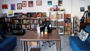 A room with a wooden table, bookshelves, a blue sofa, and various artworks on the walls. - Hostel YEK (Santa Ana)