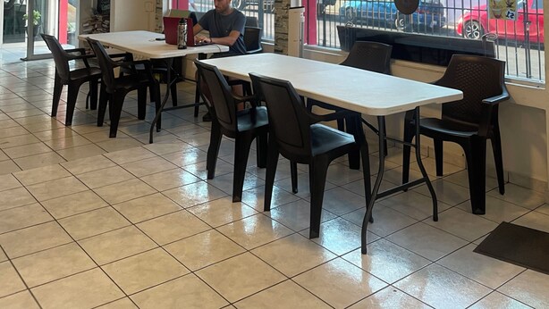 A restaurant interior with tiled floors, tables, chairs, and a person working at a computer. - Hostel YEK (Santa Ana)