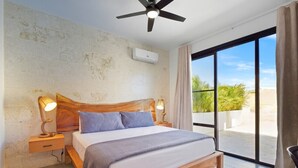 A bedroom with a wooden bed, a ceiling fan, an air conditioning unit, a nightstand with a lamp, and a large sliding glass door leading to an outdoor area.