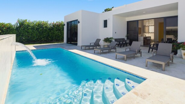 A modern pool area with a clear blue pool, lounge chairs, and a white building with large windows.