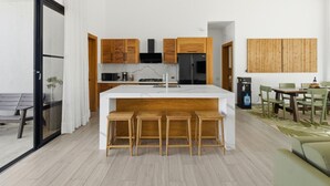 A modern kitchen with wooden cabinets, a central island with stools, and a dining area with a table and chairs.