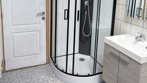 Une salle de bain avec une douche à parois de verre, un lavabo blanc et un sol carrelé.