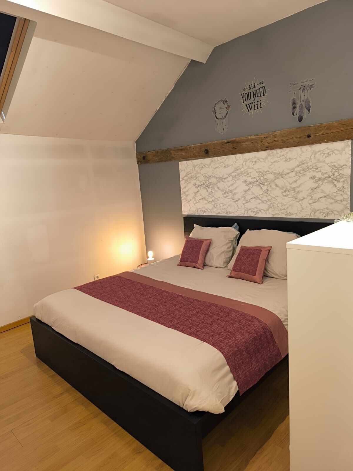 A bedroom with a bed, a headboard, a wall with a decorative sign, and a window.