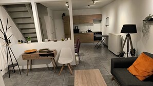 Un salon moderne comprenant un canapé, une table basse, une table à manger et des chaises. Un escalier mène à un niveau supérieur.