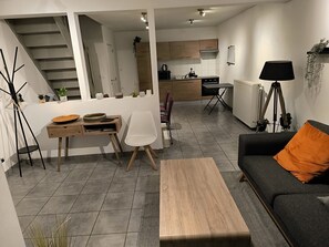 Un salon moderne comprenant un canapé, une table basse, une table à manger et des chaises. Un escalier mène à un niveau supérieur.