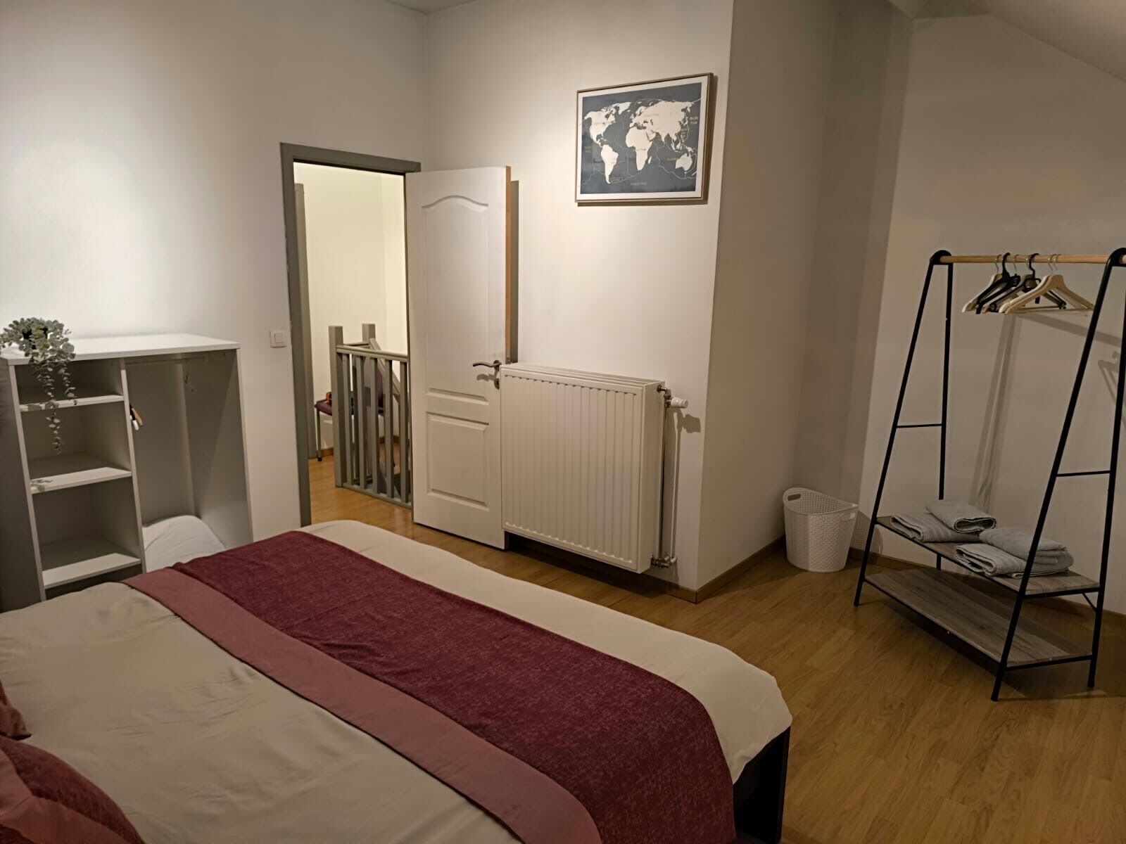 Et soveværelse med seng, garderobe, radiator, verdenskort og tøjstativ.