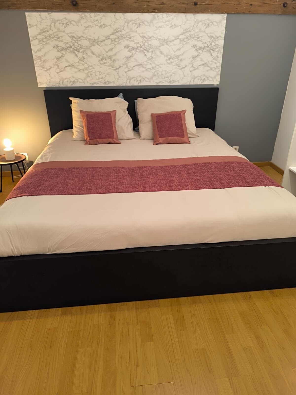 A bed with a dark headboard, a marble-patterned wall above, and a wooden floor.