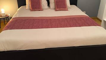 A bed with a dark headboard, a marble-patterned wall above, and a wooden floor.