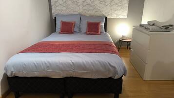 A neatly made bed with a headboard, a small bedside table with a lamp, and a dresser.