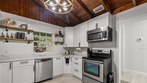 Een moderne keuken met witte kasten, roestvrijstalen apparatuur en een houten plafond.