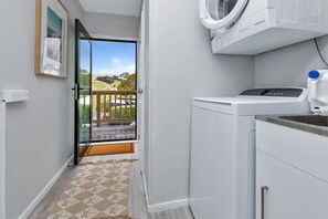 A laundry room with a washing machine, a dryer, and a sink. There is a door leading to a balcony with a view of houses and a road. - Langs Beach Coastal Getaway - Walk to Beach (Langs Beach)