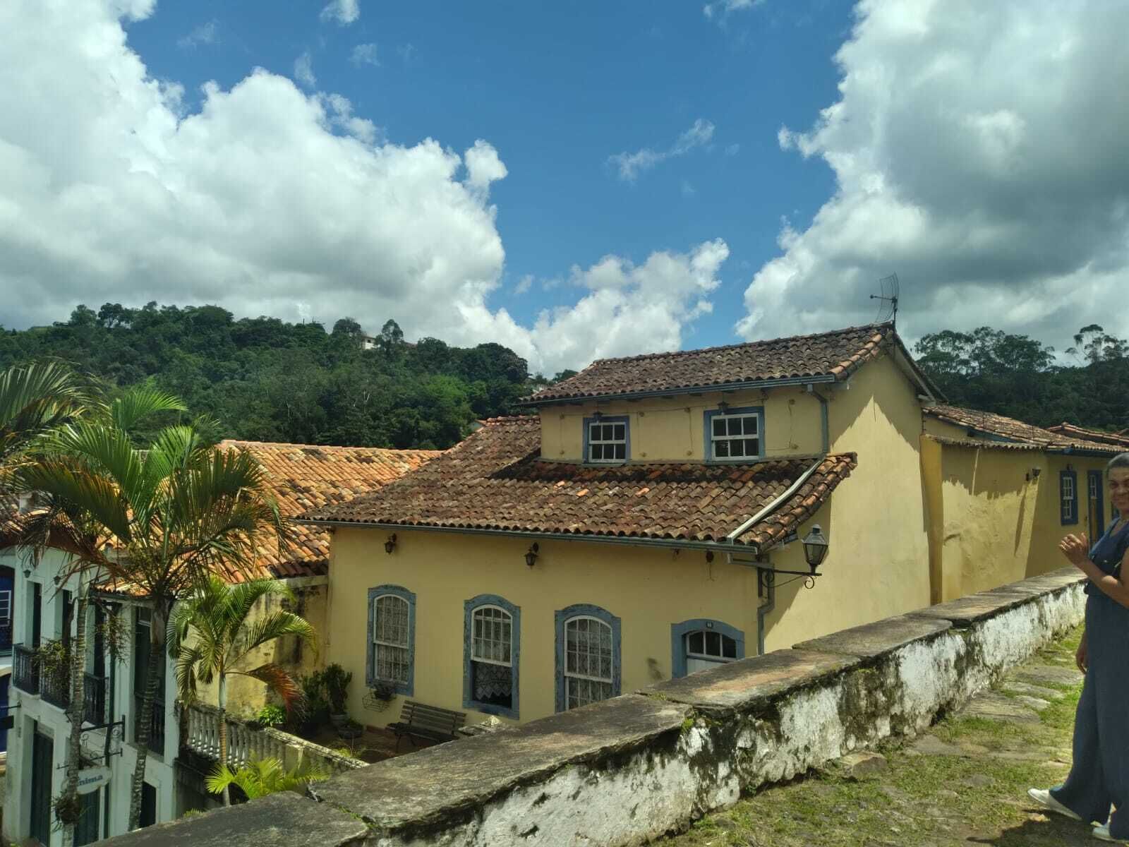 Un edificio de dos pisos con techo de tejas, un balcón y vistas a una colina verde exuberante.