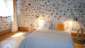 Ein Schlafzimmer mit einer Wand im Steinoptik, einem Bett mit weißen und gelben Kissen und zwei Nachttischlampen.