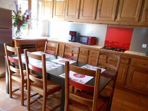 A kitchen with wooden cabinets, a dining table with chairs, a microwave, and a gas stove. - Le Sancy Cézallier - COMPAINS (COMPAINS)