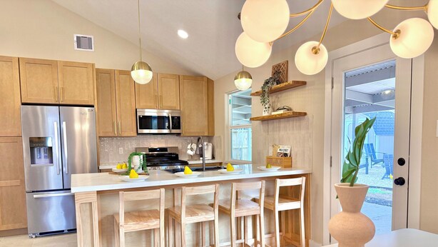 Una cocina moderna con electrodomésticos de acero inoxidable, armarios de madera y una isla central con taburetes de bar.