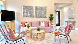 Una sala de estar con un sofá, dos sillones de mimbre, una mesa de centro y un televisor.