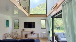 A modern living room with a large TV, wooden beams, a sofa, a small table, and a view of greenery. - Villa Vaimoeani + bungalow  - pool - serenity in Moorea, Haapiti - 8 pers (Haapiti)
