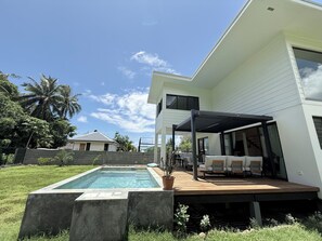 Et moderne hus med swimmingpool, udendørs møbler og en overdækket terrasse.