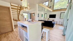 A modern interior with a central island, a staircase, a flat-screen TV, and a view of a green landscape. - Villa Vaimoeani + bungalow  - pool - serenity in Moorea, Haapiti - 8 pers (Haapiti)