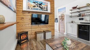 A modern kitchen with a TV, wooden wall paneling, a fireplace, and a dining area with a wooden table. - Steps to Terrace Beach & Trails • Whale’s Tail (Ucluelet)